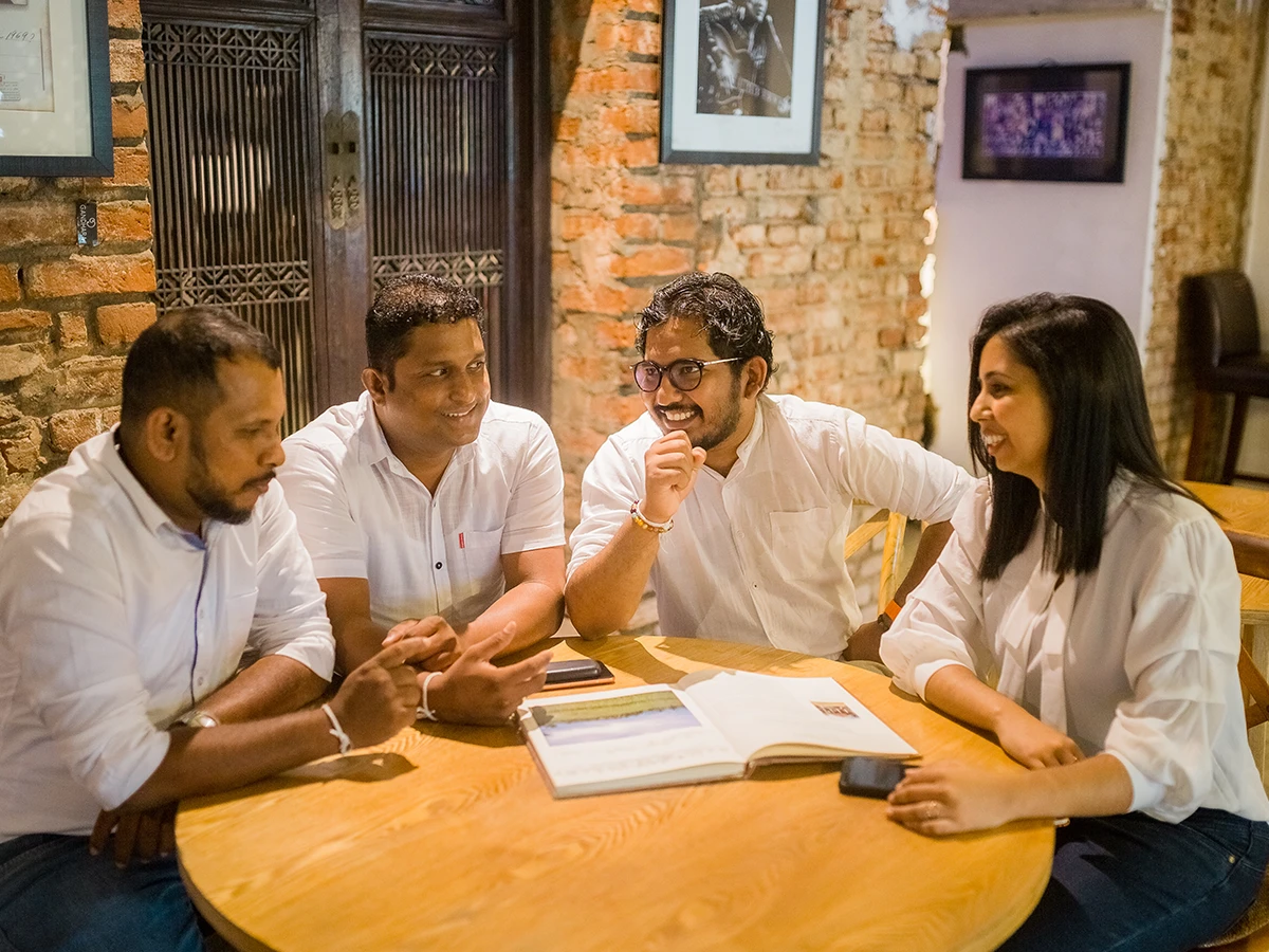 Four of the team around a round timber table, a brick wall behind