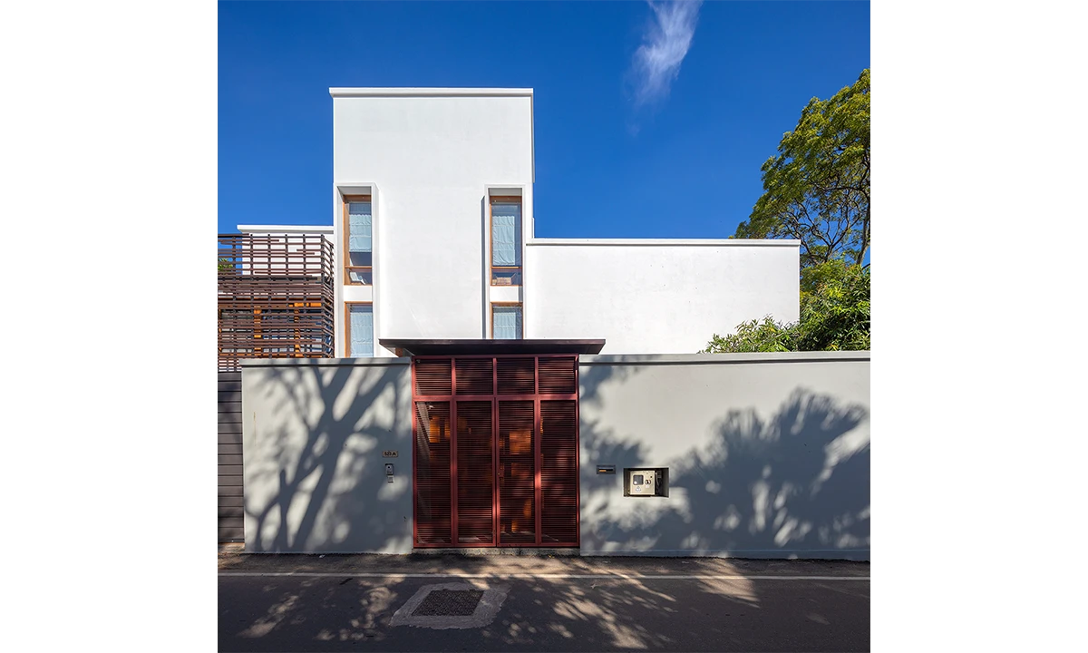 Street front of the House at Colombo: white volumes behind a boundary wall with a red timber gate