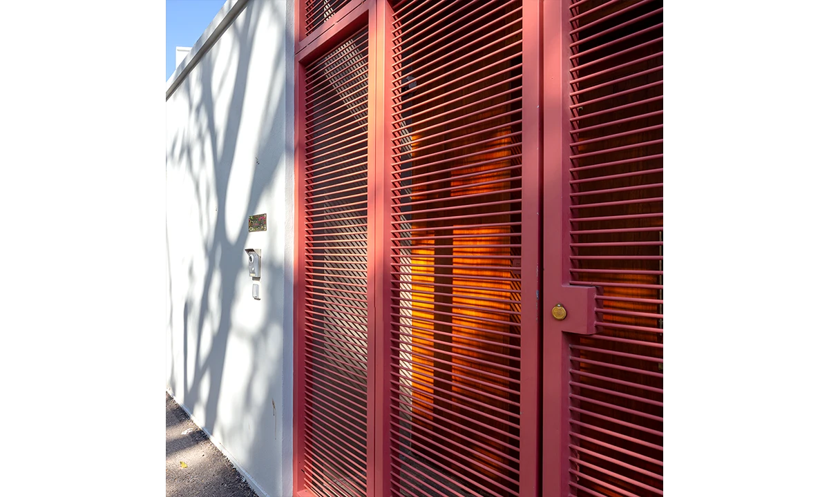 Red louvred timber gate against a white wall