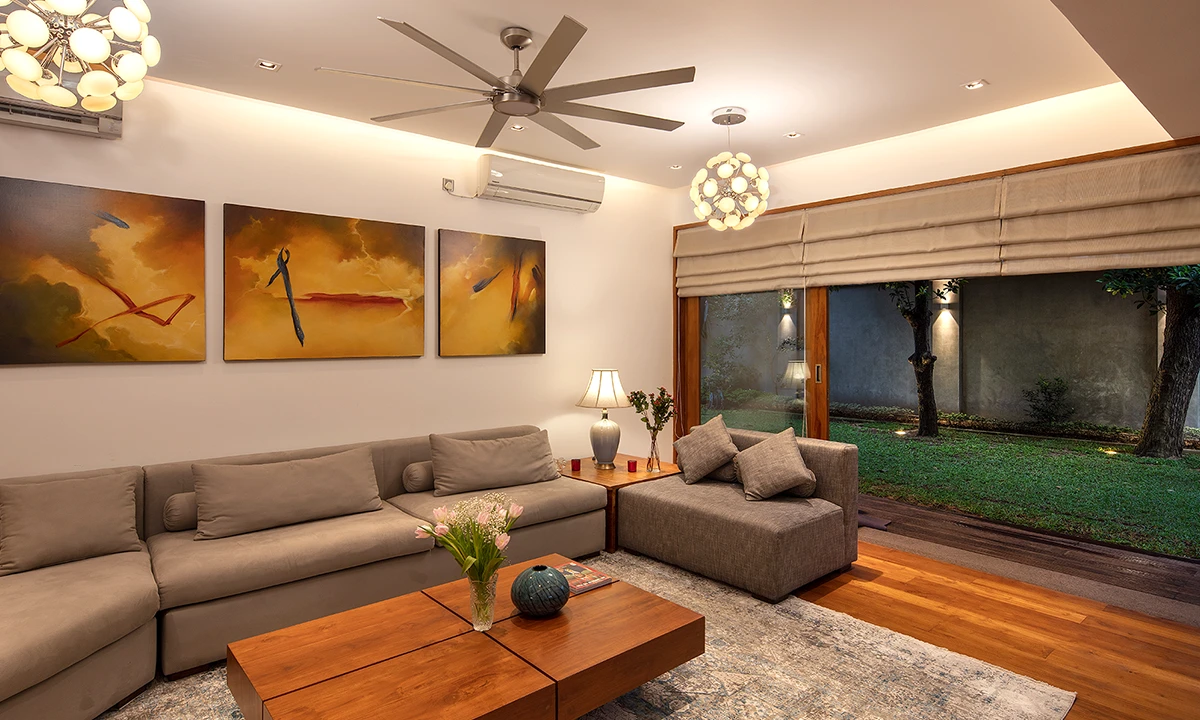 Living room with a sectional sofa, a timber coffee table and three abstract paintings, facing the garden