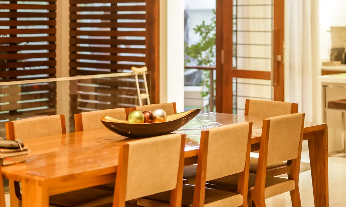 Timber dining table and chairs beside tall louvred timber shutters