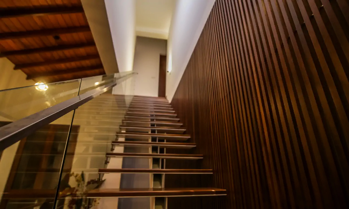 Timber stair with a glass balustrade beside a wall of vertical timber slats