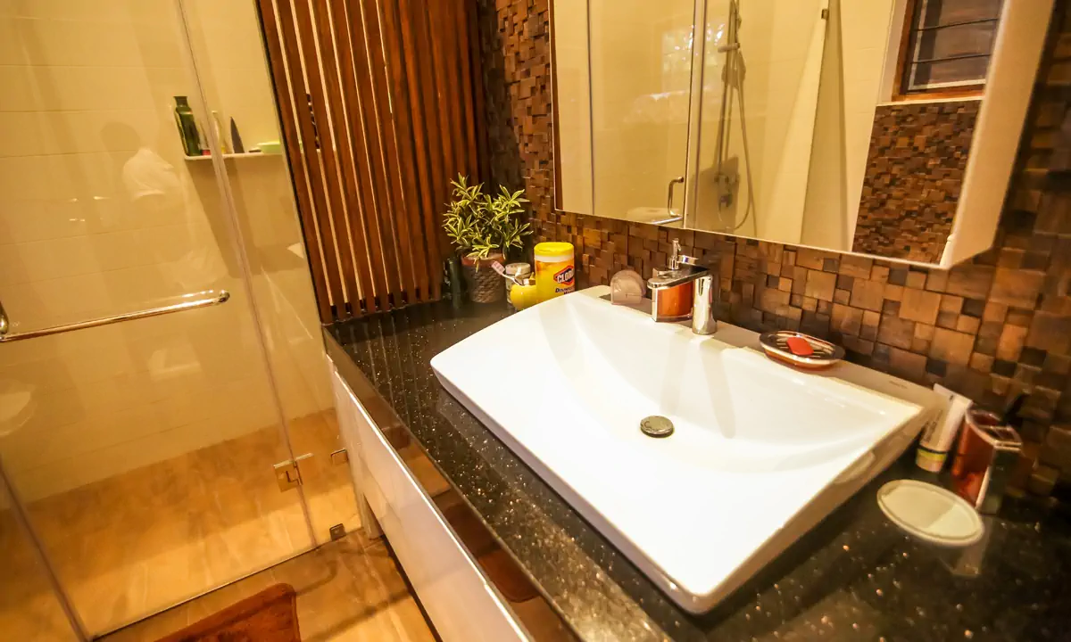 Bathroom with a white basin on a black granite counter and a glass shower