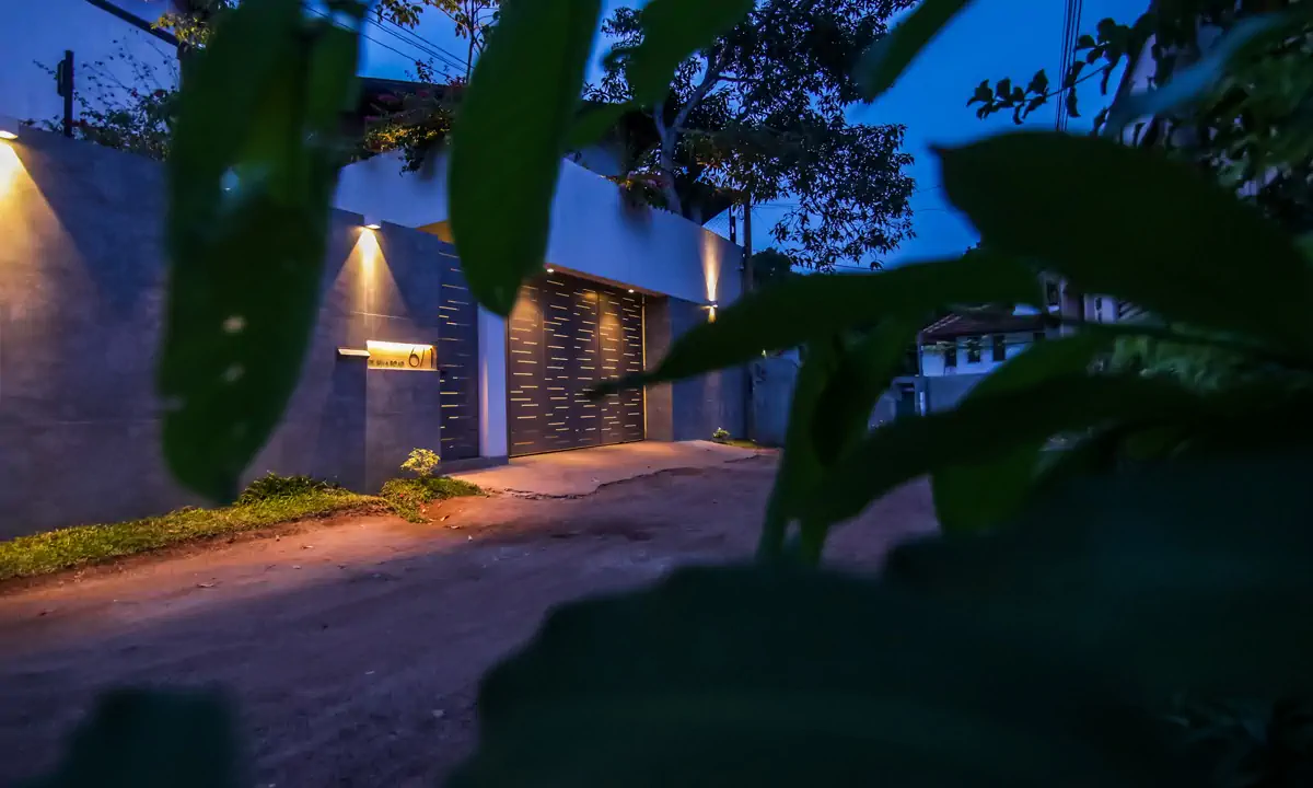 The grey boundary wall and gate lit at dusk, seen from the lane