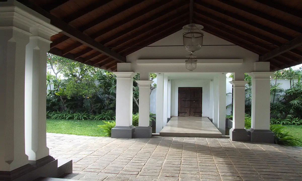Open entrance pavilion under a timber roof, white columns framing the walk to the door
