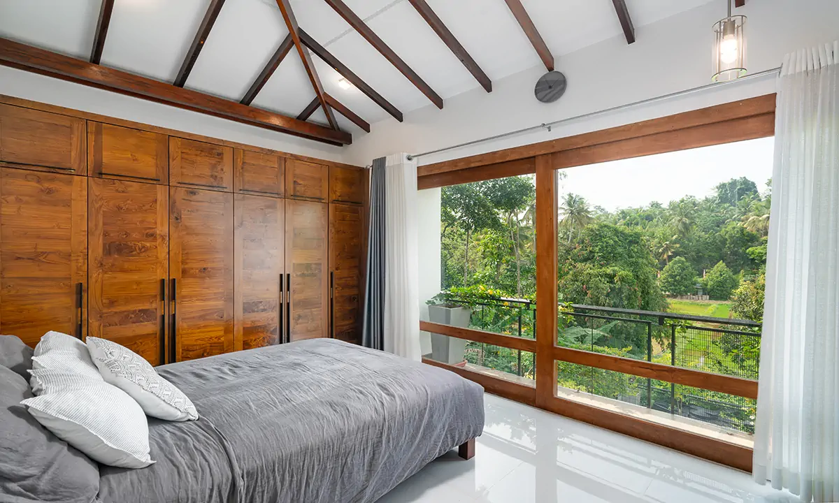Bedroom with timber wardrobes and a wide timber-framed window onto the trees