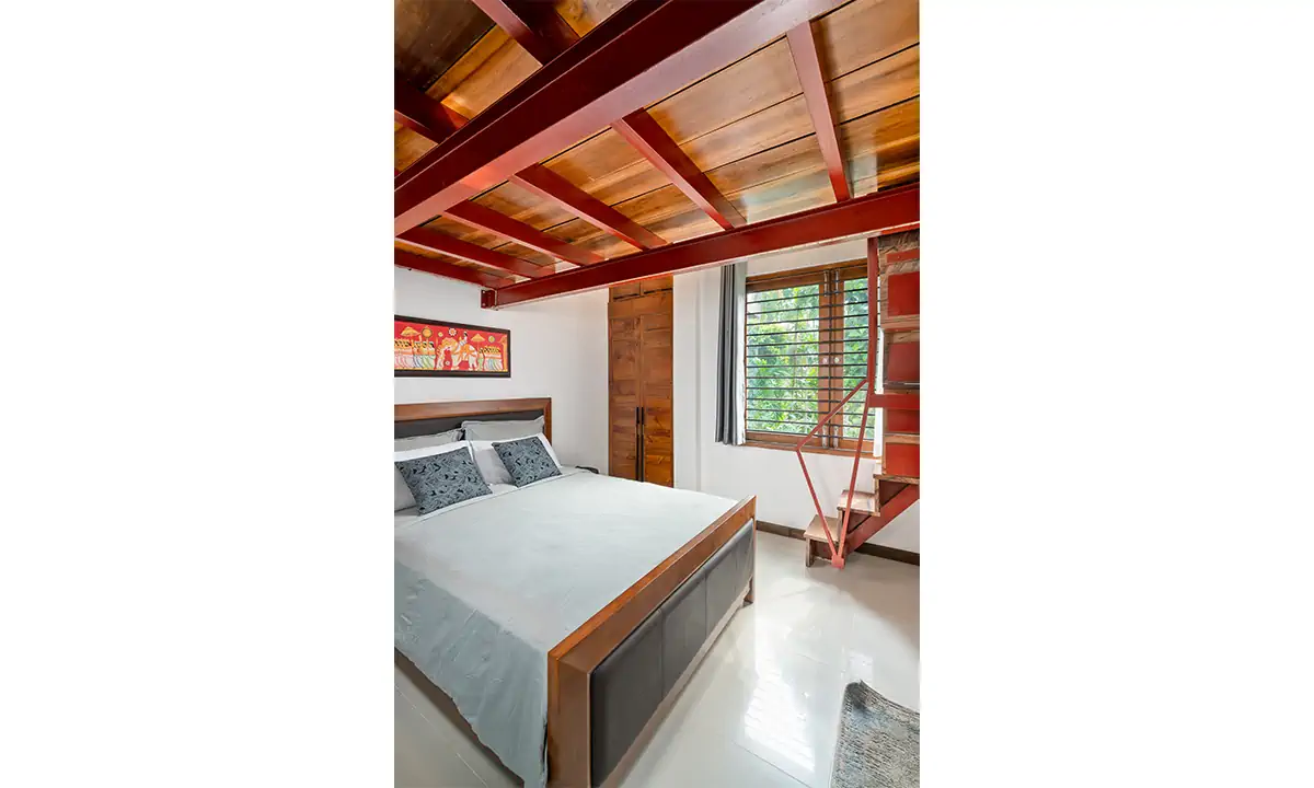Bedroom beneath exposed rafters, with a steel ladder up to a loft