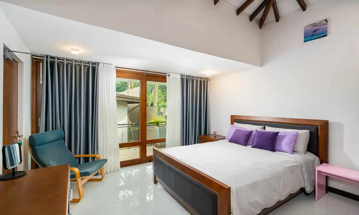 Bedroom with a timber bed, a blue armchair and glass doors to a balcony