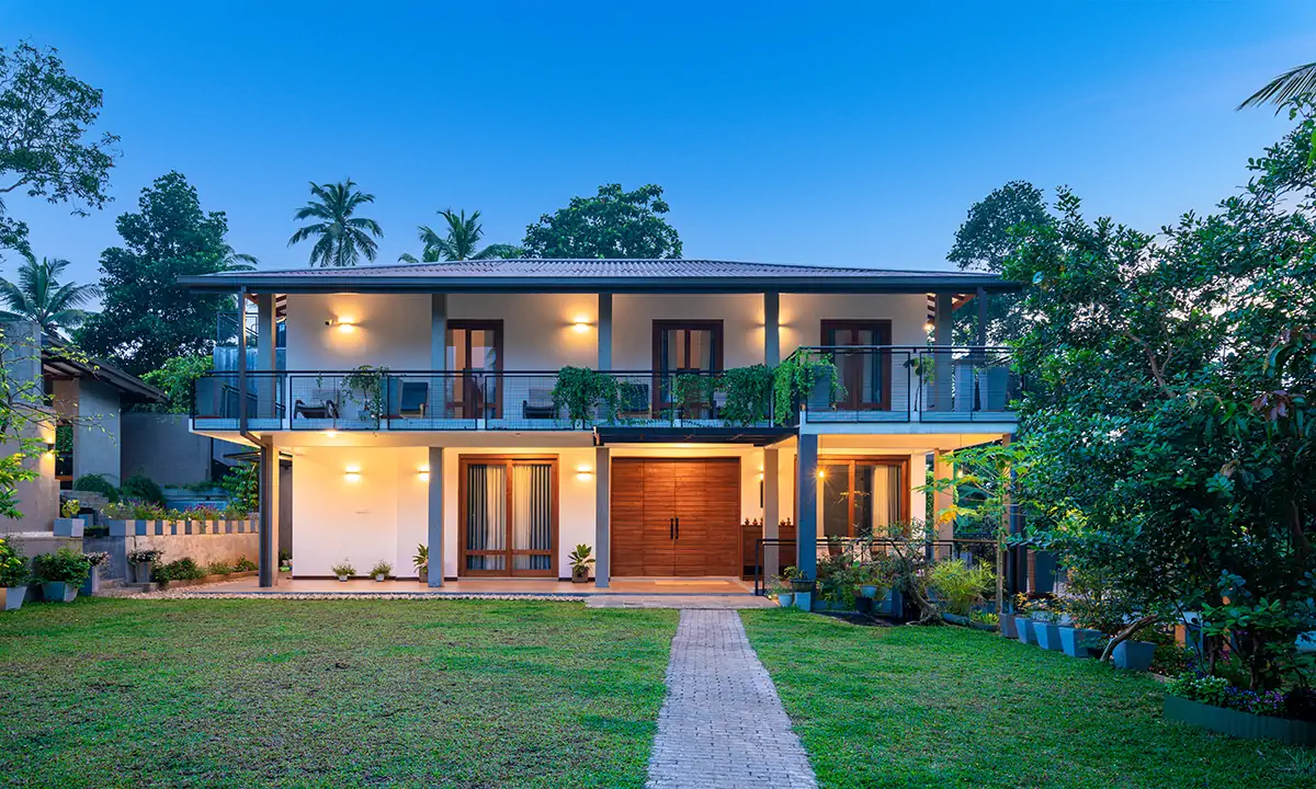 The house at dusk from the front lawn, with its long first-floor balcony and timber door