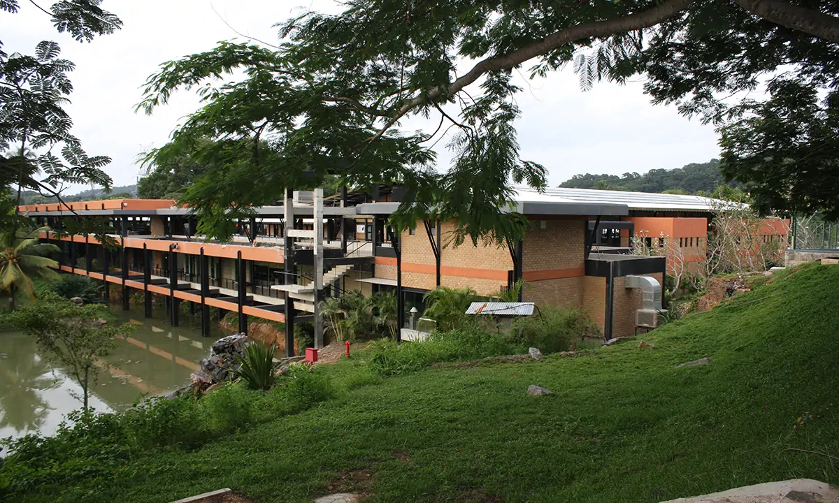 The factory’s long buildings along the water, from a grassy bank