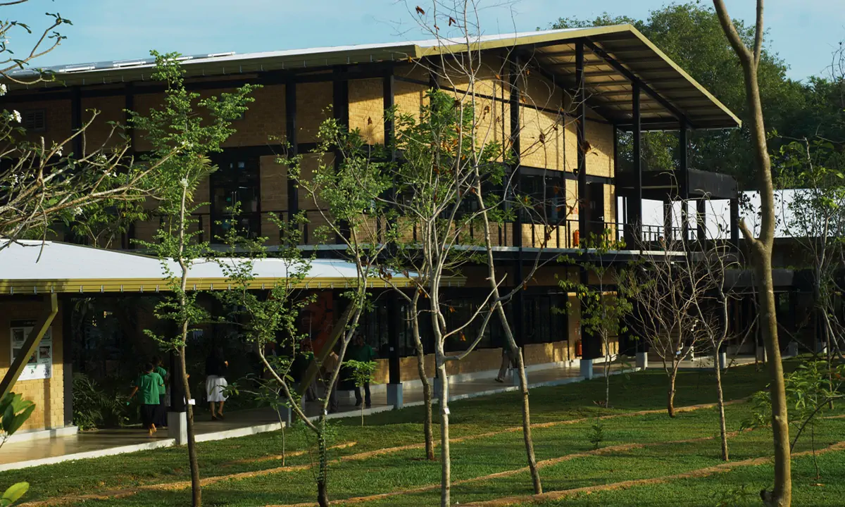 Two-storey block with a deep overhanging roof and an exposed steel frame, beyond young trees
