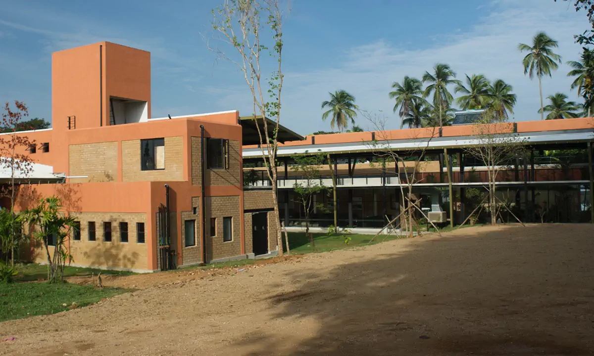 Terracotta-coloured block and long factory roofs, with coconut palms behind