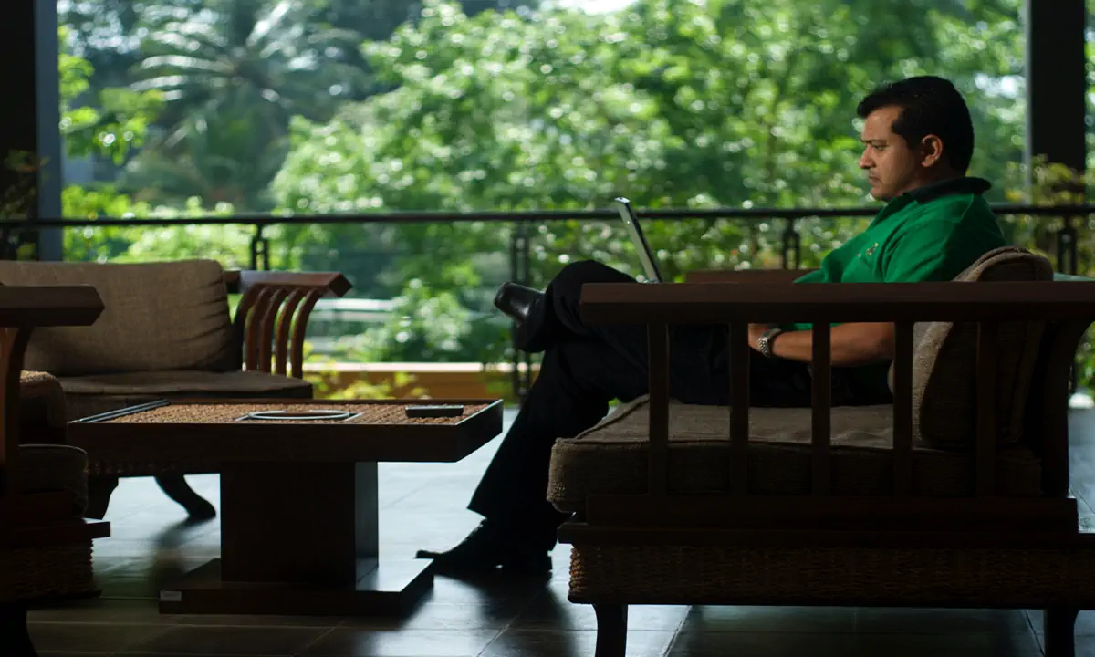 A man working on a laptop in a lounge open to the trees