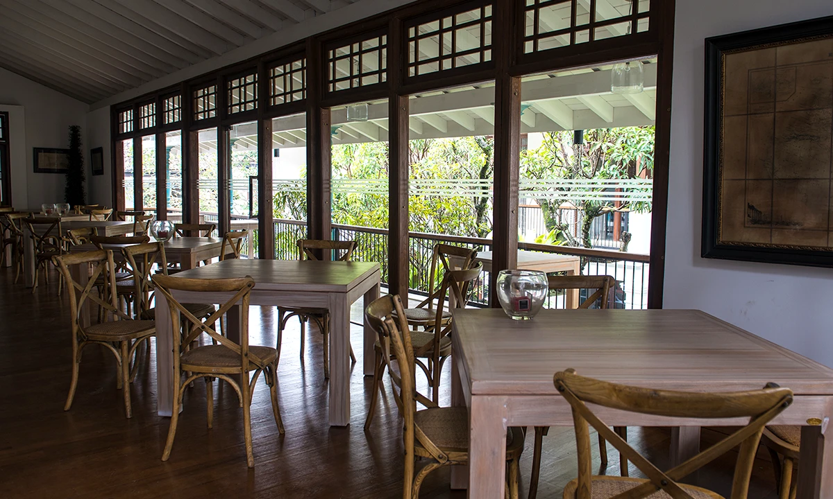 Dining room with timber tables and cross-back chairs, glazed timber screens open to the garden