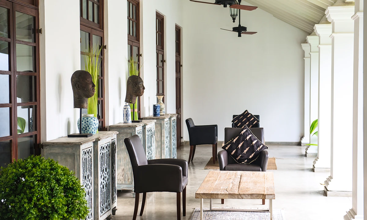 Long verandah lounge with white columns, carved cabinets and leather armchairs