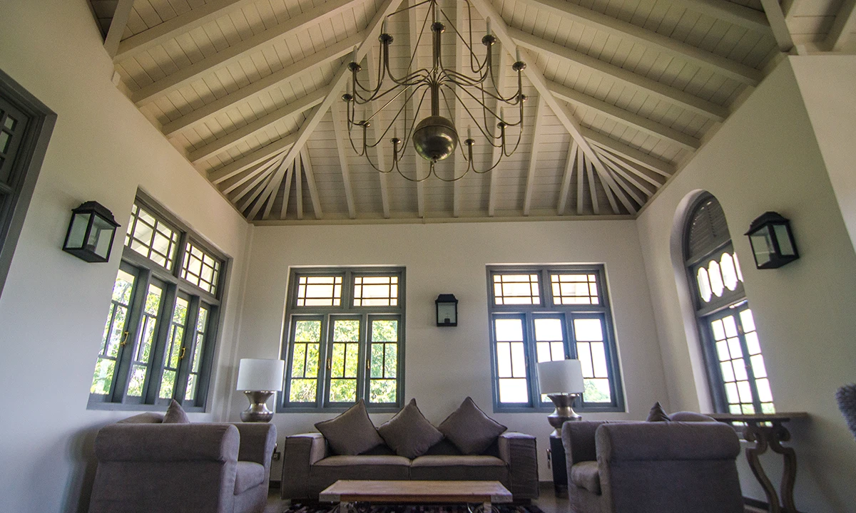 Living room under a white-painted timber roof, with a chandelier and arched windows