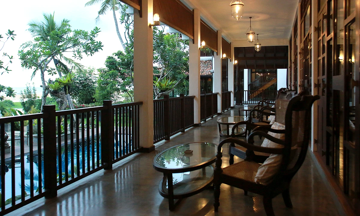 Verandah with timber armchairs and a glass-topped table beside the balustrade